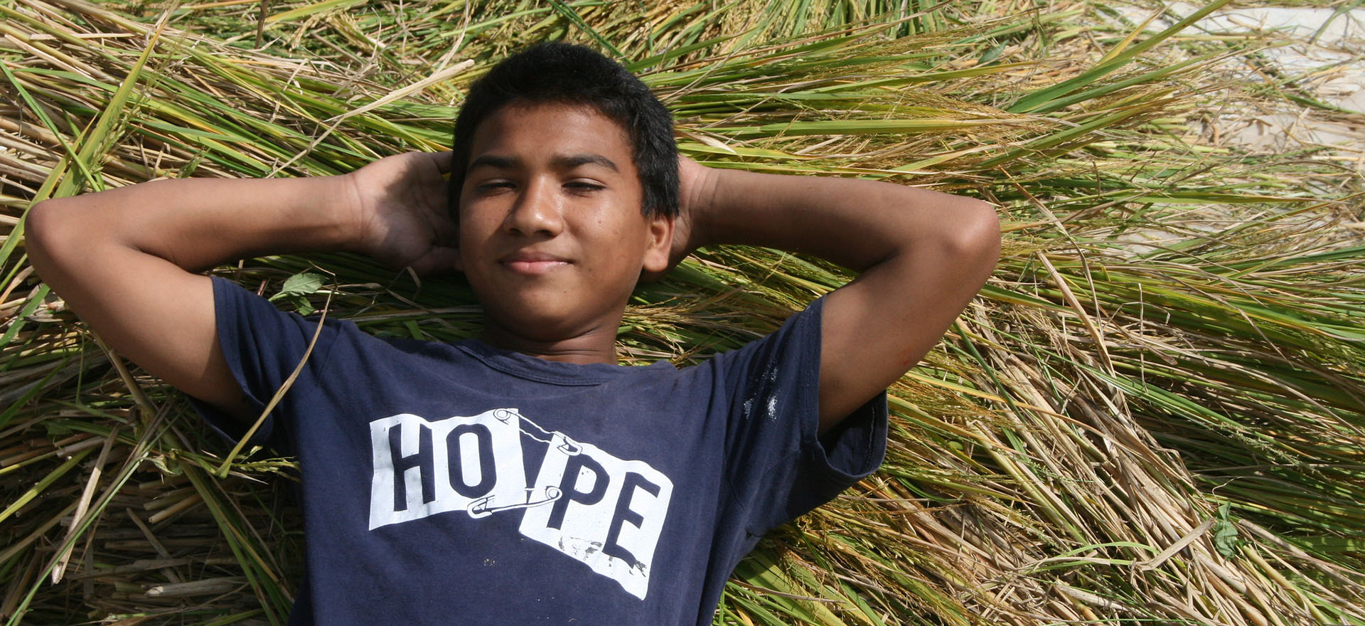ama ghar child resting on dried grass with a shirt that says hope