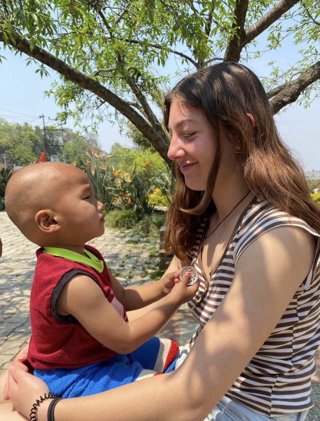 Bérénice holds the youngest Ama Ghar child, Pasang on her lap while Pasang plays with her necklace.