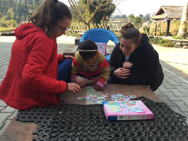 Two teenage girls with a young girl between them work on a puzzle.